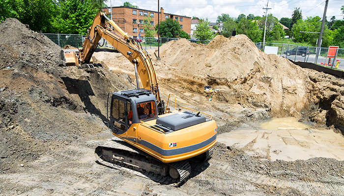 A large construction excavator removes contaminated soil from an urban brownfield development site.